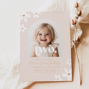 May include: A pink and white birthday invitation with a photo of a young child. The invitation says "Please join us to celebrate Olivia's Second Birthday" and includes the date, time, and location of the party. The invitation is decorated with white daisies with gold centers.