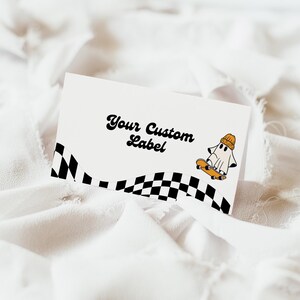 May include: White card with black and white checkered border and a ghost wearing a yellow beanie riding a skateboard. The text "Your Custom Label" is written in a retro font.