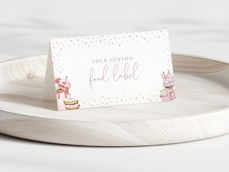 May include: A white card with a pink border and pink sprinkles. The card says "Your Custom Food Label" in pink script. There are illustrations of donuts, cupcakes, and milkshakes on the card.