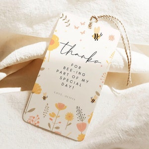 May include: A white thank you tag with a floral pattern and bee illustrations. The text reads "Thanks for bee-ing part of my special day! Love, Olivia."