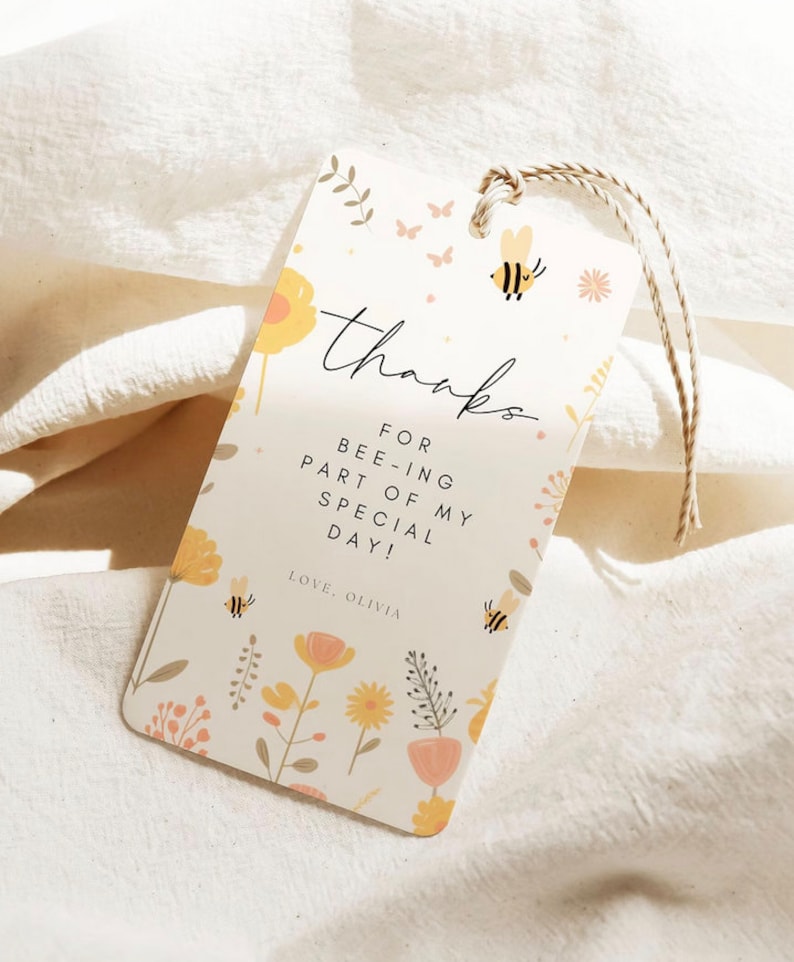 May include: A white thank you tag with a floral pattern and bee illustrations. The text reads "Thanks for bee-ing part of my special day! Love, Olivia."