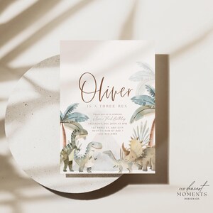 K&ouml;nnte beinhalten: Eine hellrosa Dinosaurier-Geburtstagseinladung mit einer Aquarell-Illustration von Dinosauriern und Palmen. Der Text lautet "Oliver ist ein Three Rex" und enth&auml;lt Details zur Party, einschlie&szlig;lich Datum, Uhrzeit und Ort.