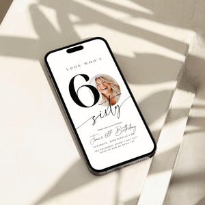 May include: A smartphone displays a birthday invitation. The invitation reads "Look Who's Sixty" with a photo of a smiling woman. The invitation includes the date, time, and location of the event.