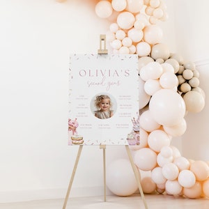 May include: A pink and white printable sign with a photo of a young girl and the text "Olivia's second year". The sign has sections for "I am", "I can", "I love", "Fav book", "Fav toys", and "Fav foods".