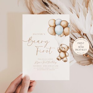 May include: A printable invitation for a first birthday party with a teddy bear holding balloons. The invitation is decorated with a watercolor illustration of a teddy bear holding balloons in shades of brown and blue. The text on the invitation reads "Oliver's Beary First" and includes the date and time of the party.