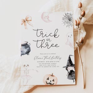May include: A Halloween-themed birthday invitation with a watercolour illustration of a witch, a ghost, a pumpkin, a cauldron, a spider web, and a bow. The text reads "Trick or Three, Olivia's Third Birthday, Saturday, June 26th at 4 PM, 123 Anywhere Street, Any City, Any State, RSVP to Sarah by June 1st, our dearest Moments Design Co."