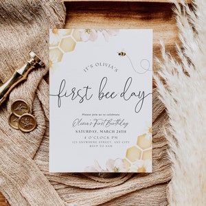 May include: A white invitation card with a bee and honeycomb design. The text reads "It's Olivia's First Bee Day". The invitation details a first birthday party for Olivia on Saturday, March 24th at 4:00 PM. The address is 123 Anywhere Street, Any City. RSVP to Sam.