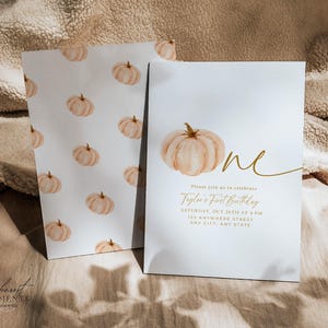 Pu&ograve; includere: Due biglietti bianchi a tema zucca. Un biglietto presenta una zucca ad acquerello e la parola "one" in corsivo dorato. L'altro biglietto ha un motivo di zucche. Il testo sul biglietto recita "Taylor's First Birthday".