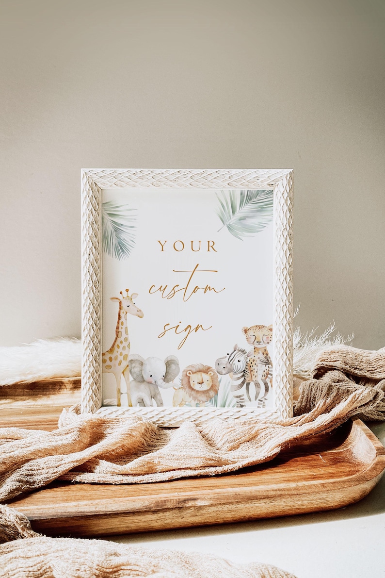 May include: A white frame with a white mat and a gold inscription that reads "YOUR custom sign". The frame features a watercolor illustration of a giraffe, elephant, lion, zebra, and leopard against a green palm leaf background.