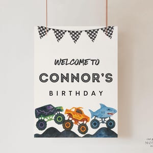 May include: A white poster with the text "Welcome to Connor's Birthday" and three monster truck illustrations. The trucks are purple, orange, and blue, with black and white checkered flags at the top.