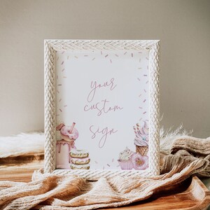 May include: White frame with a pink and white custom sign that says "your custom sign". The sign is decorated with pink and white sprinkles and illustrations of cupcakes, donuts, and milkshakes.