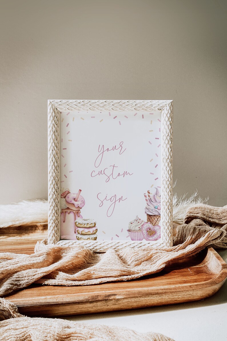 May include: White frame with a pink and white custom sign that says "your custom sign". The sign is decorated with pink and white sprinkles and illustrations of cupcakes, donuts, and milkshakes.