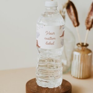 May include: A clear plastic water bottle with a white label that says "Your custom label". The label has a pattern of brown cowboy boots and cacti. The bottle is sitting on a wooden coaster.
