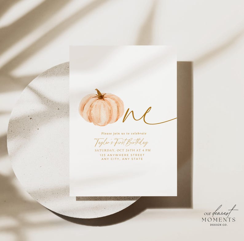 Pu&ograve; includere: Un biglietto d'invito bianco con un'illustrazione di zucca ad acquerello e testo dorato. Il testo recita "One", "Taylor's First Birthday" e i dettagli dell'evento. Il design include le parole "Our Dearest Moments Design Co."