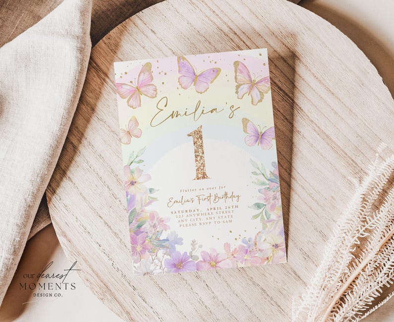 May include: A pastel-colored invitation card for a first birthday celebration. The card features the name "Emilia's" in gold script, a large glittery gold number "1", and delicate butterfly and floral illustrations. The card includes event details.