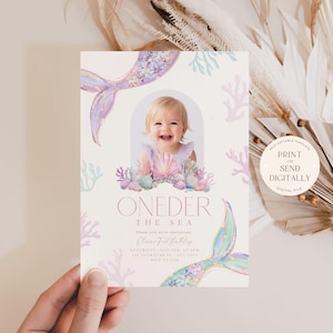 May include: A printable invitation for a first birthday party with a mermaid theme. The invitation features a watercolor illustration of a mermaid tail, coral, and seashells. The text "One-der the Sea" is written in pink and white. The invitation is designed to be printed or sent digitally.