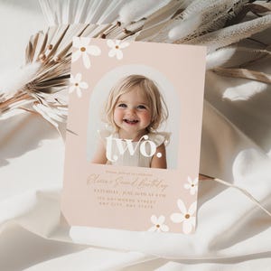 May include: A pink birthday invitation with white flowers and the word "two" in a white circle. A photo of a young girl is in the circle. The text reads "Please join us in celebrating [Name]'s Second Birthday. [Date] at [Time]. [Address]. [City, State]".