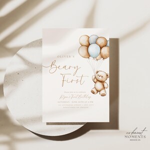 May include: A light brown teddy bear holding onto blue and brown balloons. The invitation reads "Oliver's Beary First" and includes the text "Please join us to celebrate Ryan's First Birthday, Saturday, June 24th at 4 PM, 123 Anywhere Street, Any City, Registered on Amazon".