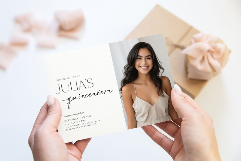 K&ouml;nnte beinhalten: Eine Quincea&ntilde;era-Einladungskarte, die von H&auml;nden gehalten wird, mit einem Foto einer l&auml;chelnden jungen Frau. Der Text der Karte lautet "YOU'RE INVITED TO JULIA'S quincea&ntilde;era" mit Veranstaltungsdetails. Eine Geschenkbox mit Schleife befindet sich im Hintergrund.