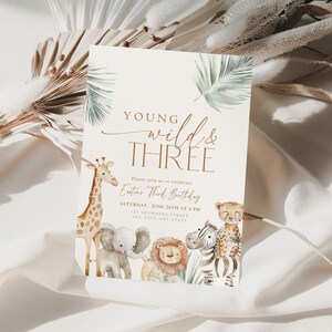 May include: A white invitation card with a jungle theme. The card features a giraffe, elephant, lion, and zebra with the text "Young Wild & Three" and "Enter Third Birthday" in gold lettering.