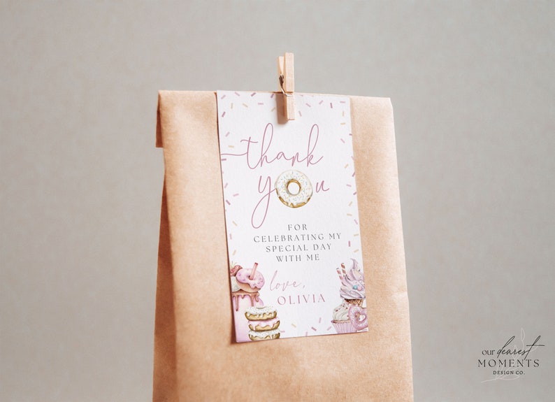 May include: A pink and white thank you tag with a donut illustration and the text "thank you" and "love, Olivia". The tag is attached to a brown paper bag with a wooden clothespin.