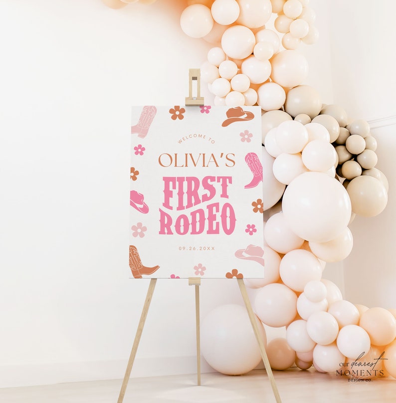 May include: A white sign with pink and brown cowboy boots, hats, and flowers. The sign says "Welcome to Olivia's First Rodeo 09.26.20XX".