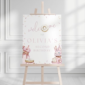 May include: Welcome to Olivia's Second Birthday party sign with a pink and white donut, sprinkles, and a cupcake with pink frosting.