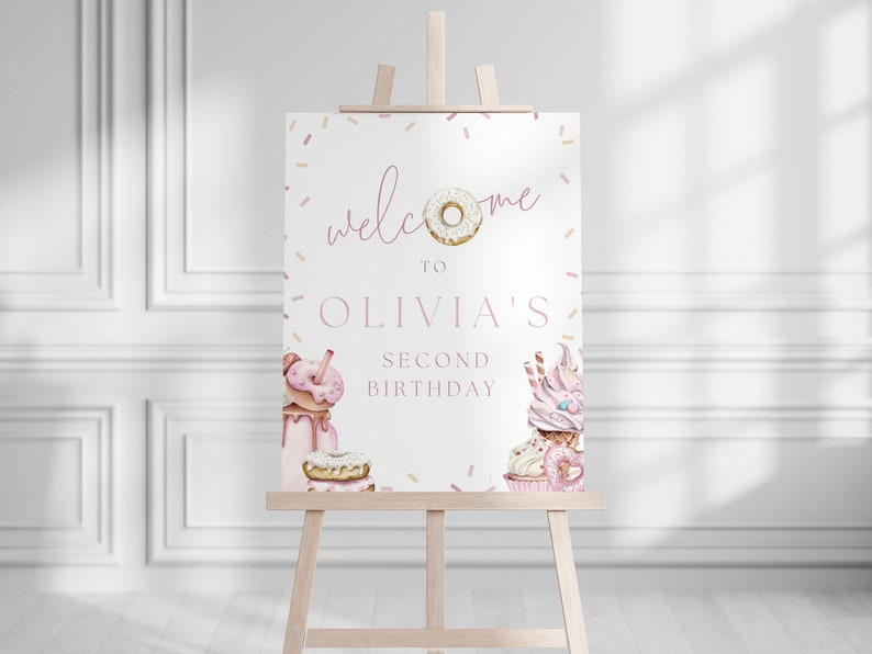 May include: Welcome to Olivia's Second Birthday party sign with a pink and white donut, sprinkles, and a cupcake with pink frosting.