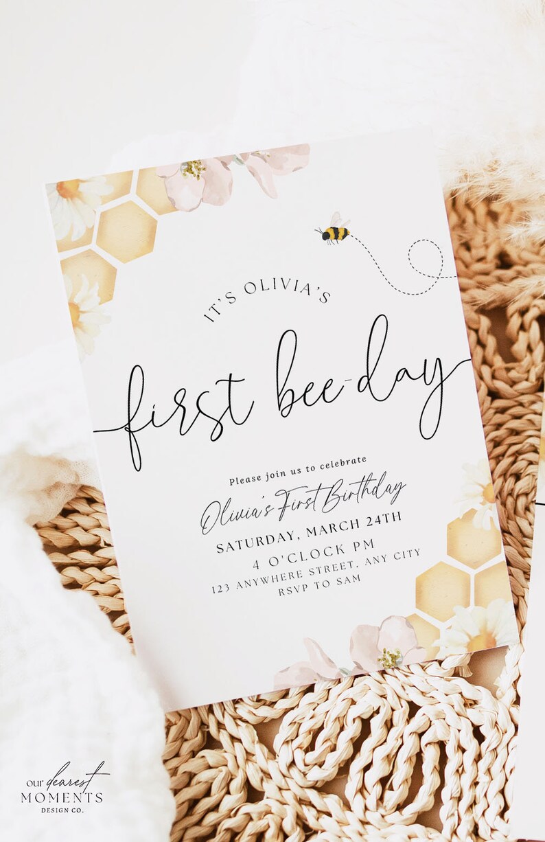 May include: A white invitation card featuring a bee and honeycomb design. The text on the card reads "It's Olivia's First Bee Day." The invitation details a first birthday party for Olivia, including the date, time, and location.