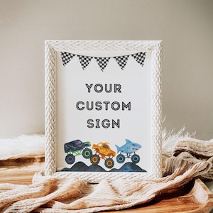 May include: White framed sign with the text "YOUR CUSTOM SIGN" and a row of monster truck illustrations. The trucks are purple, orange, and blue, with black and white checkered flags at the top.