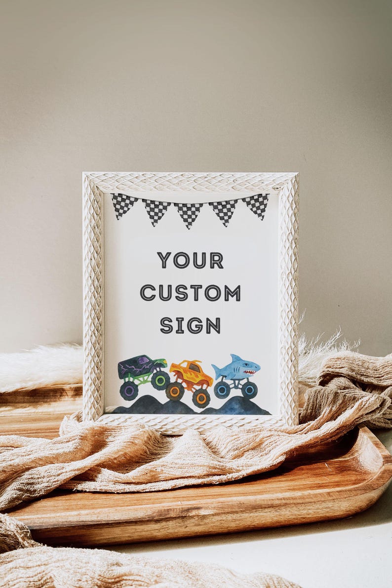 May include: White framed sign with the text "YOUR CUSTOM SIGN" and a row of monster truck illustrations. The trucks are purple, orange, and blue, with black and white checkered flags at the top.