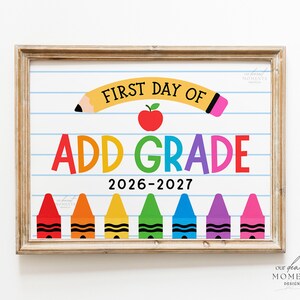 May include: A rectangular sign in a wooden frame featuring a white background with blue horizontal lines. The text reads FIRST DAY OF ADD GRADE 2026-2027. It includes a yellow pencil graphic, a red apple, and seven colourful crayons at the bottom.