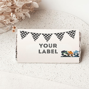 May include: A rectangular label featuring the words "YOUR LABEL" in black, decorated with a checkered flag garland and illustrations of monster trucks and a shark. The label is on a white, speckled surface.