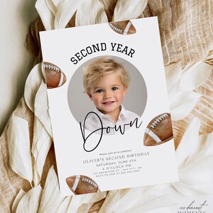 Puede incluir: Una invitación blanca con temática de fútbol para un segundo cumpleaños. La invitación presenta una foto de un niño pequeño, un gráfico de fútbol y el texto "Second Year Down".