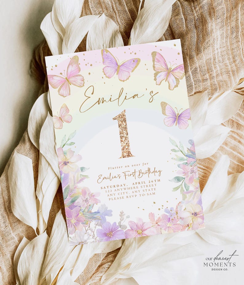 May include: A pastel-colored invitation with butterflies and floral accents. The invitation reads "Emilia's First Birthday" with the number "1" in gold glitter. The design includes the event details and the text "Our Dearest Moments Design Co."