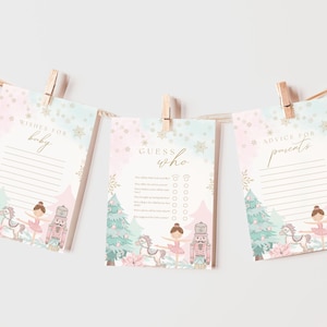 May include: Three baby shower game cards hanging from a string with wooden clothespins. The cards have a pastel pink and blue watercolor design with a ballerina, nutcracker, and Christmas tree illustration. Text on the cards includes "Wishes for baby", "Guess who", and "Advice for parents".
