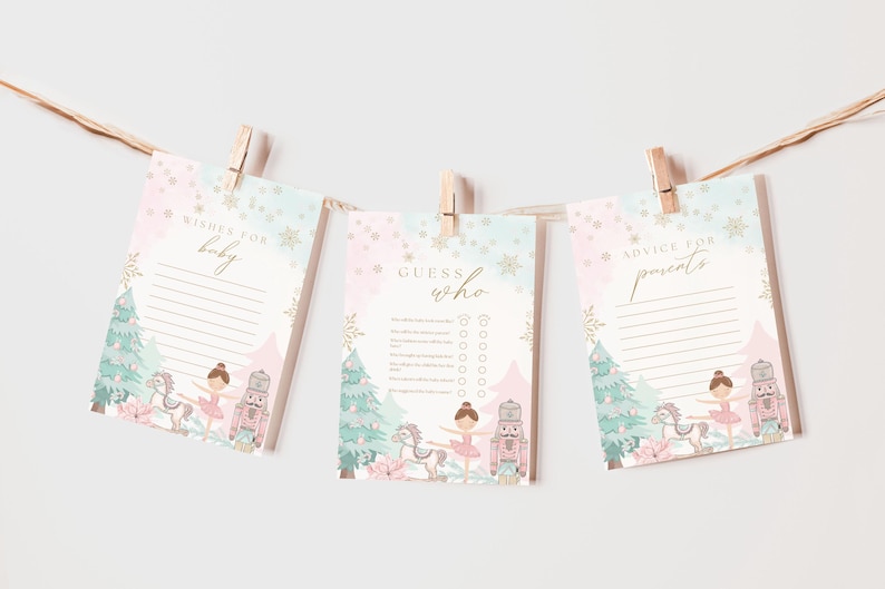 May include: Three baby shower game cards hanging from a string with wooden clothespins. The cards have a pastel pink and blue watercolor design with a ballerina, nutcracker, and Christmas tree illustration. Text on the cards includes "Wishes for baby", "Guess who", and "Advice for parents".