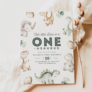 May include: A dinosaur-themed first birthday party invitation with a green and white dinosaur illustration and the text "Our little Dino is a ONE -ASAURUS". The invitation includes the date, time, and location of the party. The text "Please join us to celebrate OLIVER'S FIRST BIRTHDAY SEPT 20 2PM 123 ANYWHERE ST, ANY CITY RSVP TO SAMANTHA" is printed on the invitation. The invitation also includes the text "our dearest MOMENTS DESIGN CO."
