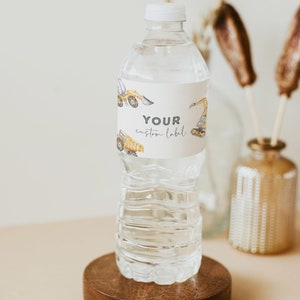 May include: A clear plastic water bottle with a white cap and a label that says "YOUR custom label". The label has a pattern of yellow construction vehicles. The bottle is sitting on a wooden coaster.