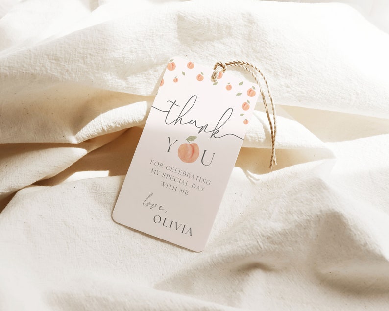 May include: Peach-themed thank you tag with the text "Thank You" and "For celebrating my special day with me. Love, Olivia". The tag is pink with peach illustrations and green leaves.
