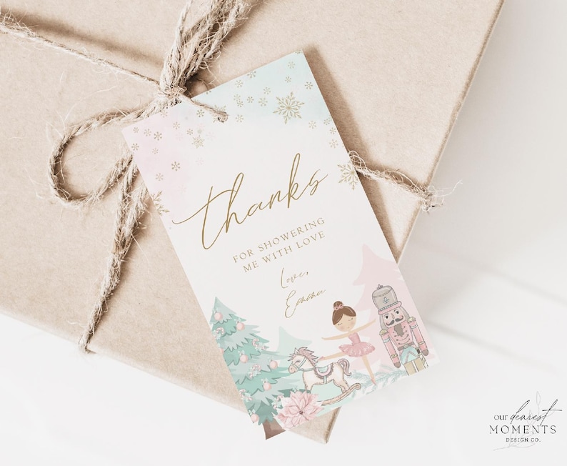 May include: A gift tag with a watercolor design featuring a ballerina, nutcracker, and rocking horse. The tag says "thanks" in gold script, with the text "for showering me with love" below. The tag is tied to a wrapped gift.