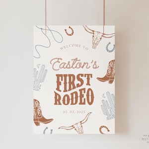 May include: White sign with brown text and illustrations. The text reads "Welcome to Easton's First Rodeo 02.03.2025". The illustrations include cacti, horseshoes, cowboy boots, and a steer skull.