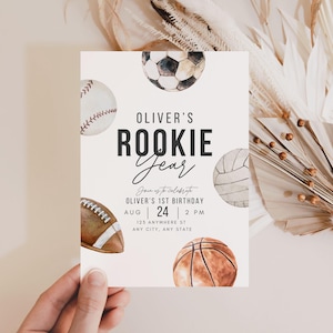May include: A white invitation card with a watercolor illustration of various sports balls, including a baseball, soccer ball, volleyball, football, and basketball. The text on the card reads "Oliver's Rookie Year" and includes details for a 1st birthday party.