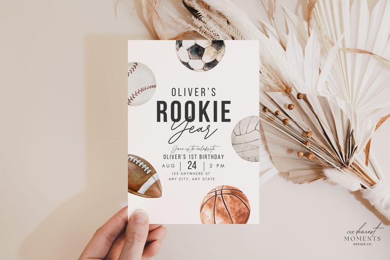 May include: A white invitation card with a watercolor illustration of various sports balls, including a baseball, soccer ball, volleyball, football, and basketball. The text on the card reads "Oliver's Rookie Year" and includes details for a 1st birthday party.