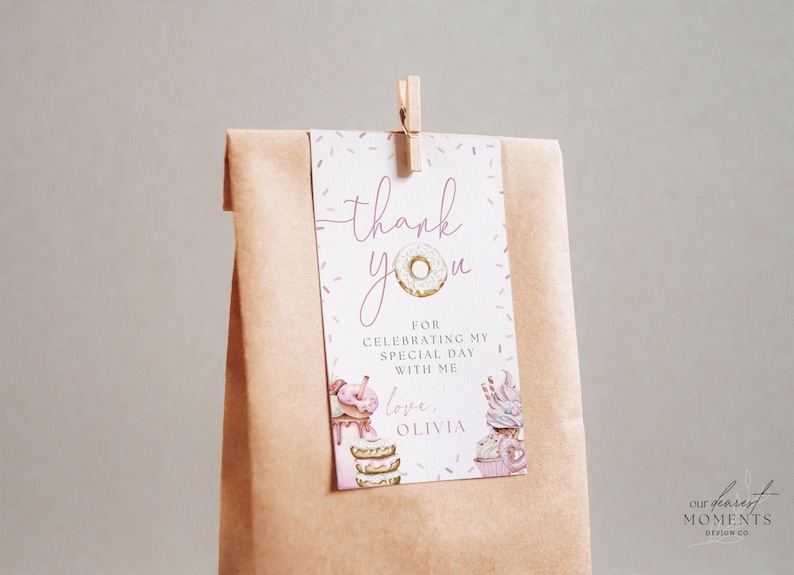 May include: A pink and white thank you tag with a donut illustration and the text "thank you" and "love, Olivia". The tag is attached to a brown paper bag with a wooden clothespin.