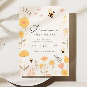 May include: A yellow and white invitation card with a bee and flowers. The text on the card reads "Olivia's First Bee Day" and includes details for Olivia's first birthday party.