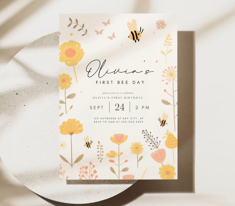 May include: A yellow and white invitation card with a bee and flowers. The text on the card reads "Olivia's First Bee Day" and includes details for Olivia's first birthday party.