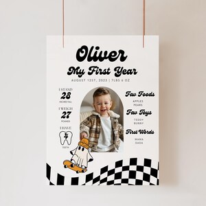 May include: A black and white checkered background with a photo of a baby boy in a brown and white sweater. The text "Oliver My First Year" is at the top of the poster. The poster also includes the baby's stats, such as height, weight, and number of teeth. The text "Fav Foods", "Fav Toys", and "First Words" are listed with examples of each.