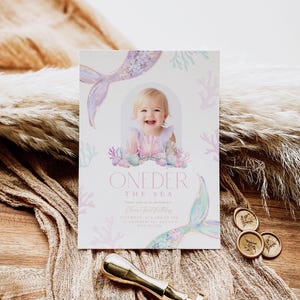 May include: A pink and blue mermaid-themed first birthday party invitation with a photo of a baby girl. The invitation says "One-der the Sea" and includes the date and time of the party.
