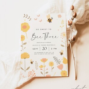 Pu&ograve; includere: Un invito bianco con un design floreale e api. Il testo recita "So Sweet to Bee Three" e include i dettagli per il terzo compleanno di Olivia.